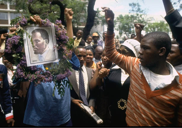 Demonstrators waving a portrait of deceased South African civil rights activist Steve Biko outside Pretoria's Old Synagogue courthouse, where the inquest into his death is taking place. Biko died while in custody of the South African Security Police.   (Photo by Sahm Doherty/Getty Images)