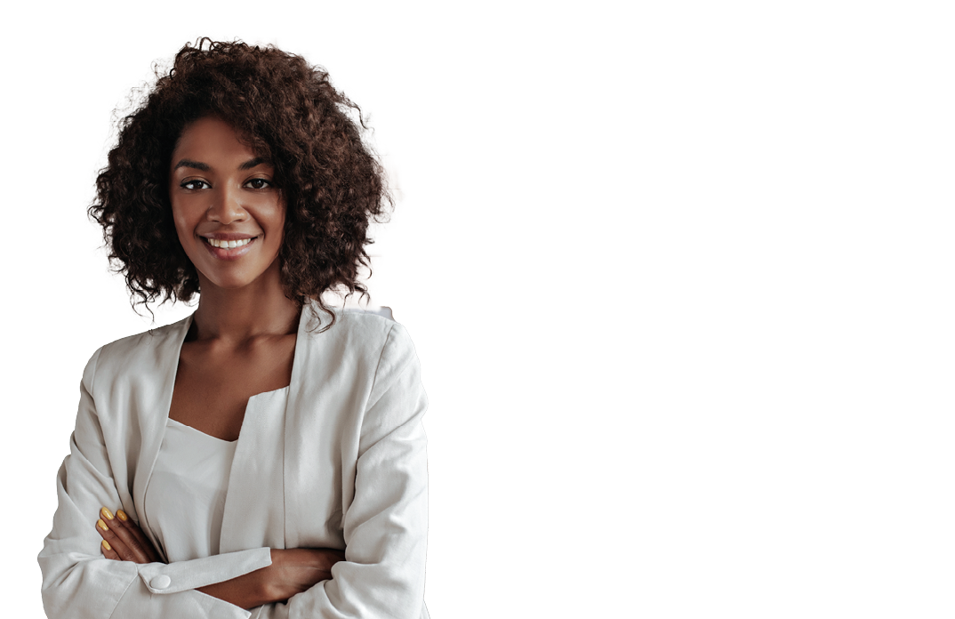 Beautiful curly brunette dark-skinned fashion designer poses in office, leans on table. Young lady in white suit crosses arms and smiles.