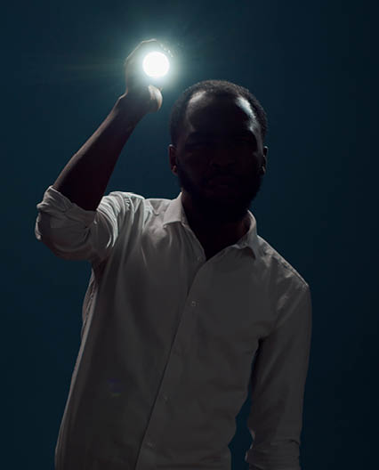 Young person sitting in the dark and using flashlight to search around, looking for evidence. Male detective taking risk and holding lantern to investigate and examine creepy sound.