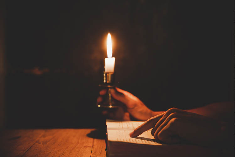 Religious man holding lit candles and reading the Holy Bible and praying in the Church, religion and faith concept