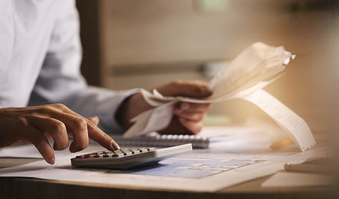 Close-up of economist using calculator while going through bills and taxes in the office.