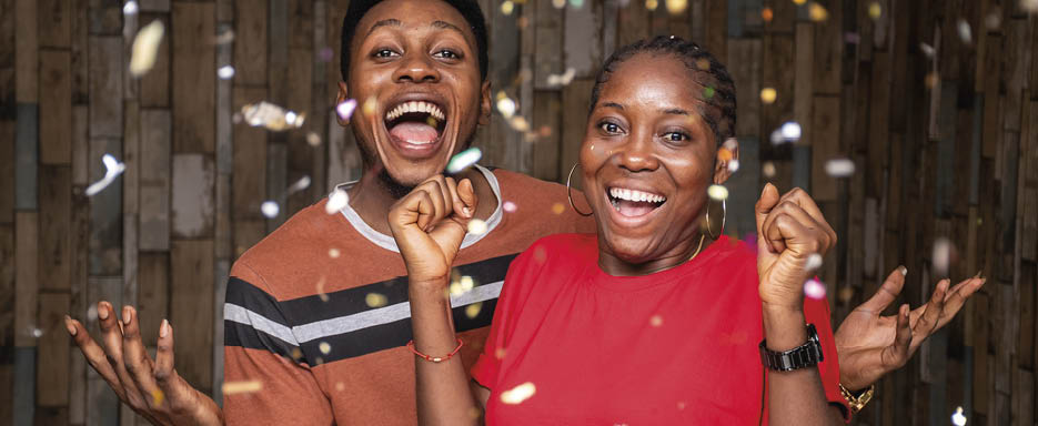 Two happy African people celebrating with confetti in front of a wooden wall